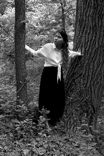 Beautiful asian girl in the woods with both hands on trees on either side of her