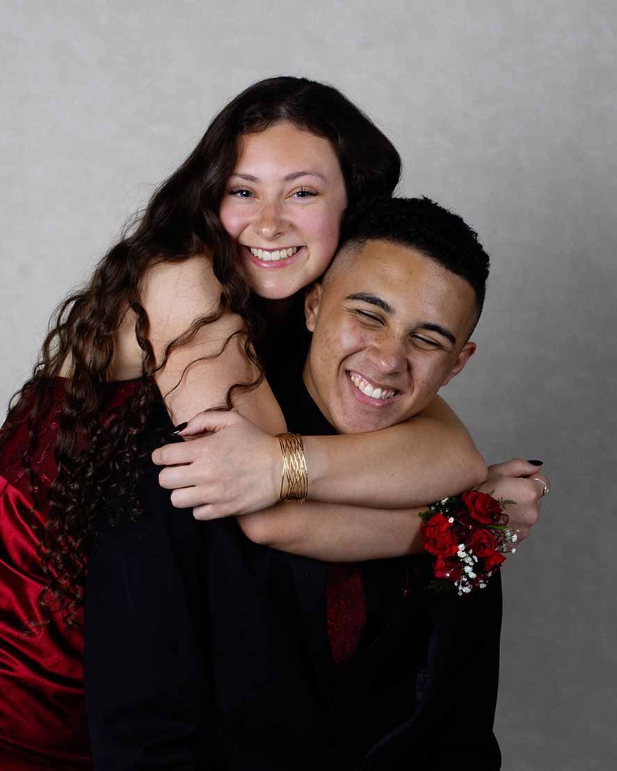 High school couple dressed for prom in studio photo. Girl is hugging boy.