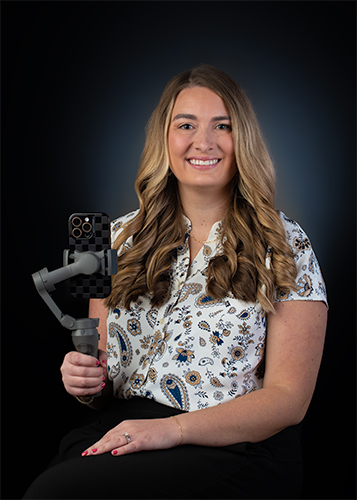 Headshot of woman in a pattern shirt holding a gimble containing a cell phone.